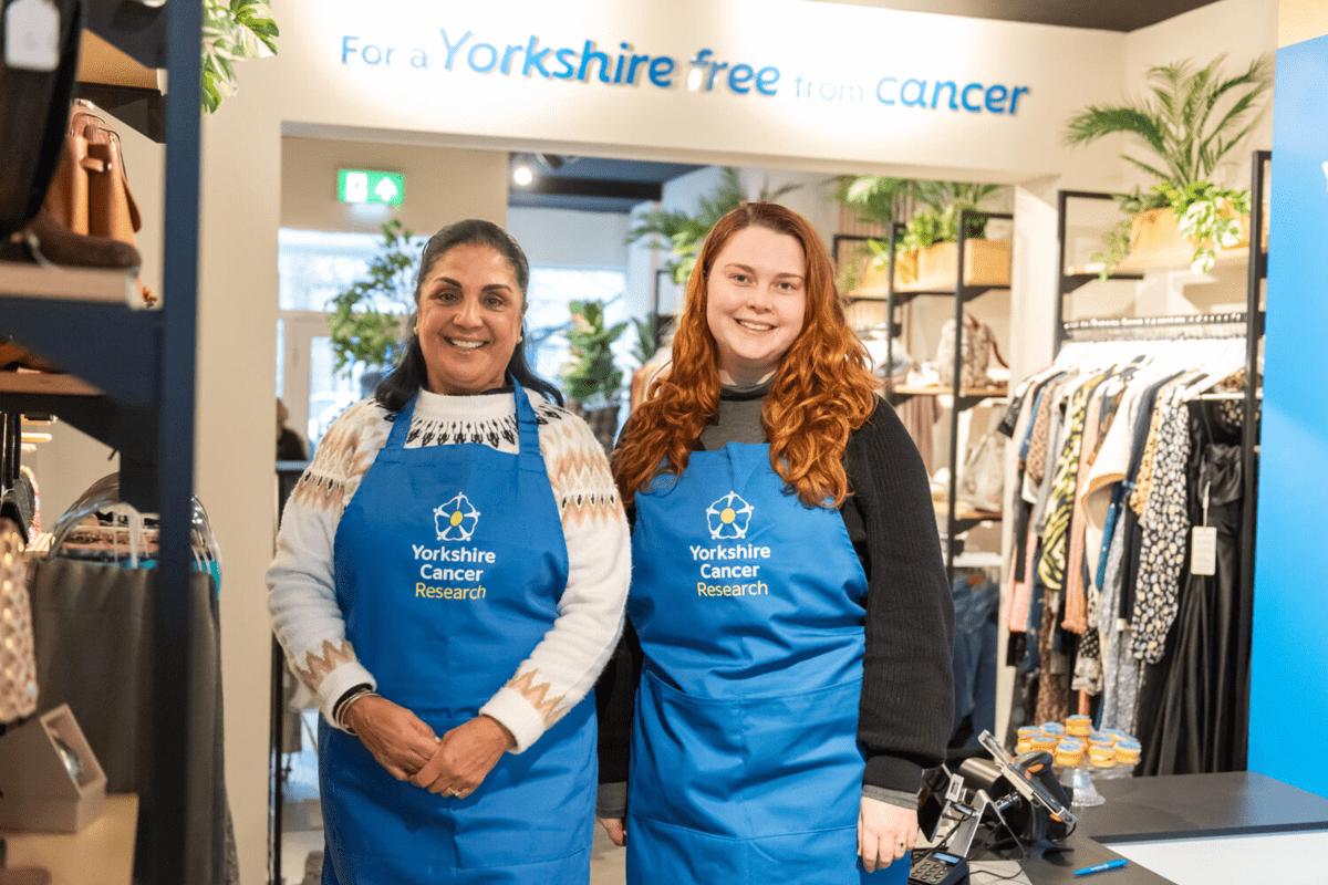 Two ladies in aprons stand in a charity shop