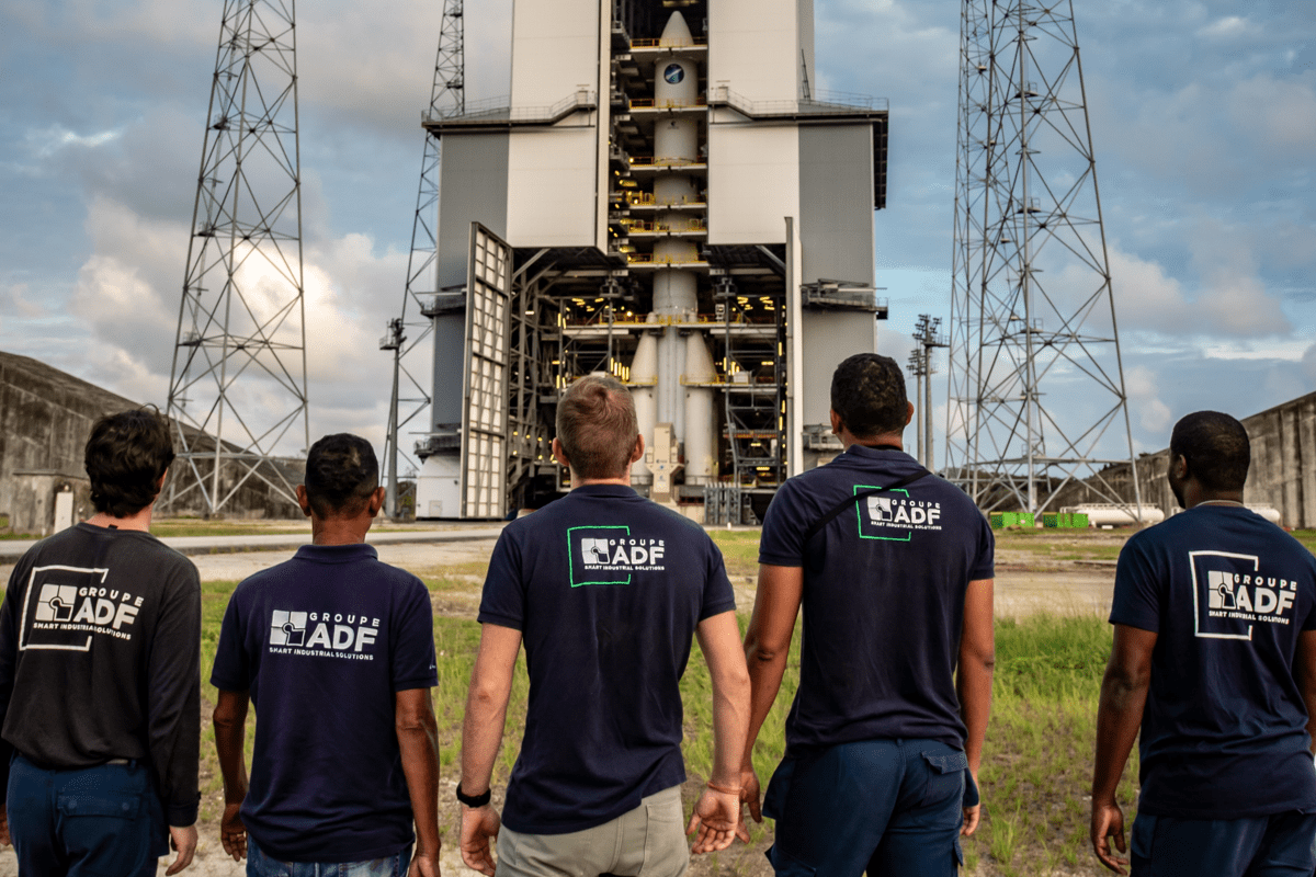 Cinco colaboradores del Groupe ADF de espaldas, contemplando el cohete Ariane en su plataforma de lanzamiento en el Centro Espacial Guayanés.