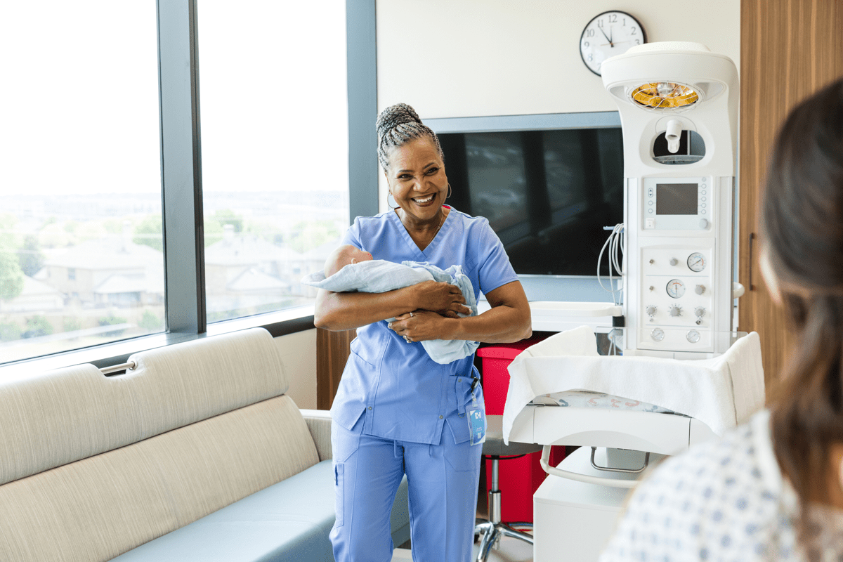 Female midwife holding a newborn, smiling. 