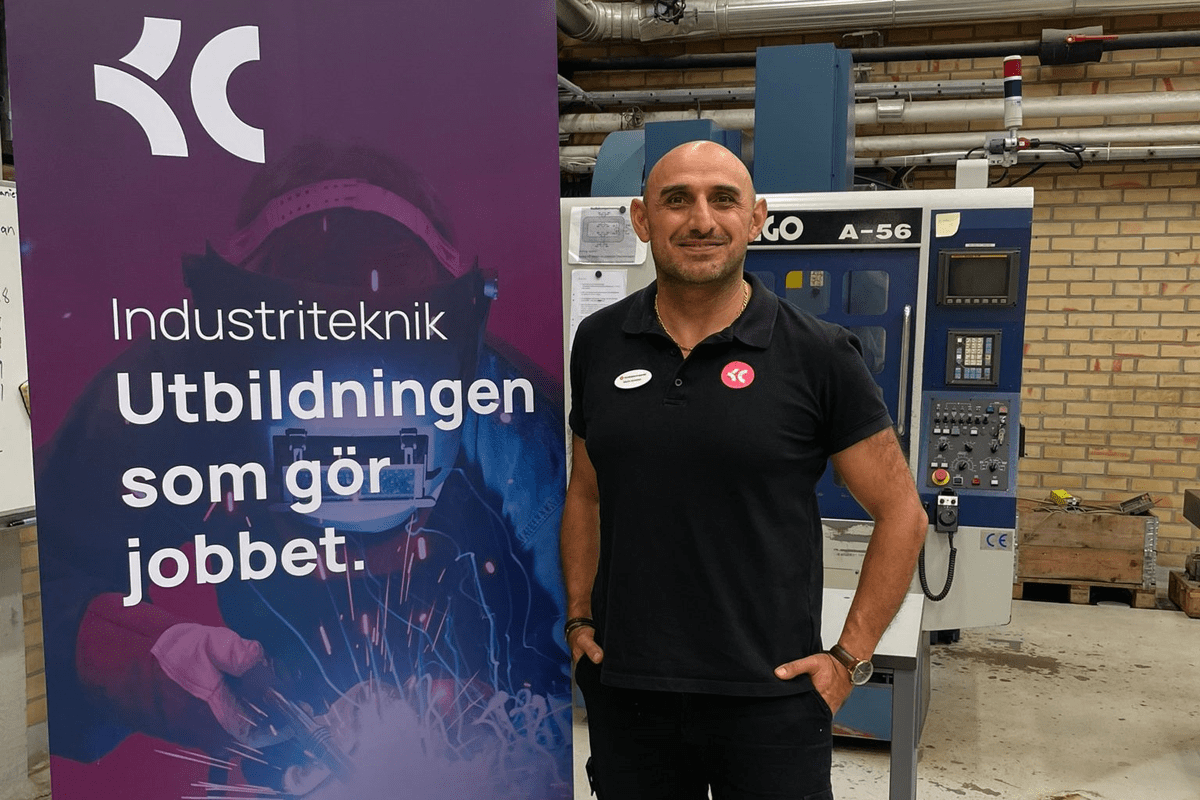 Man i svart pikétröja står bredvid en industrilärarbanderoll.
