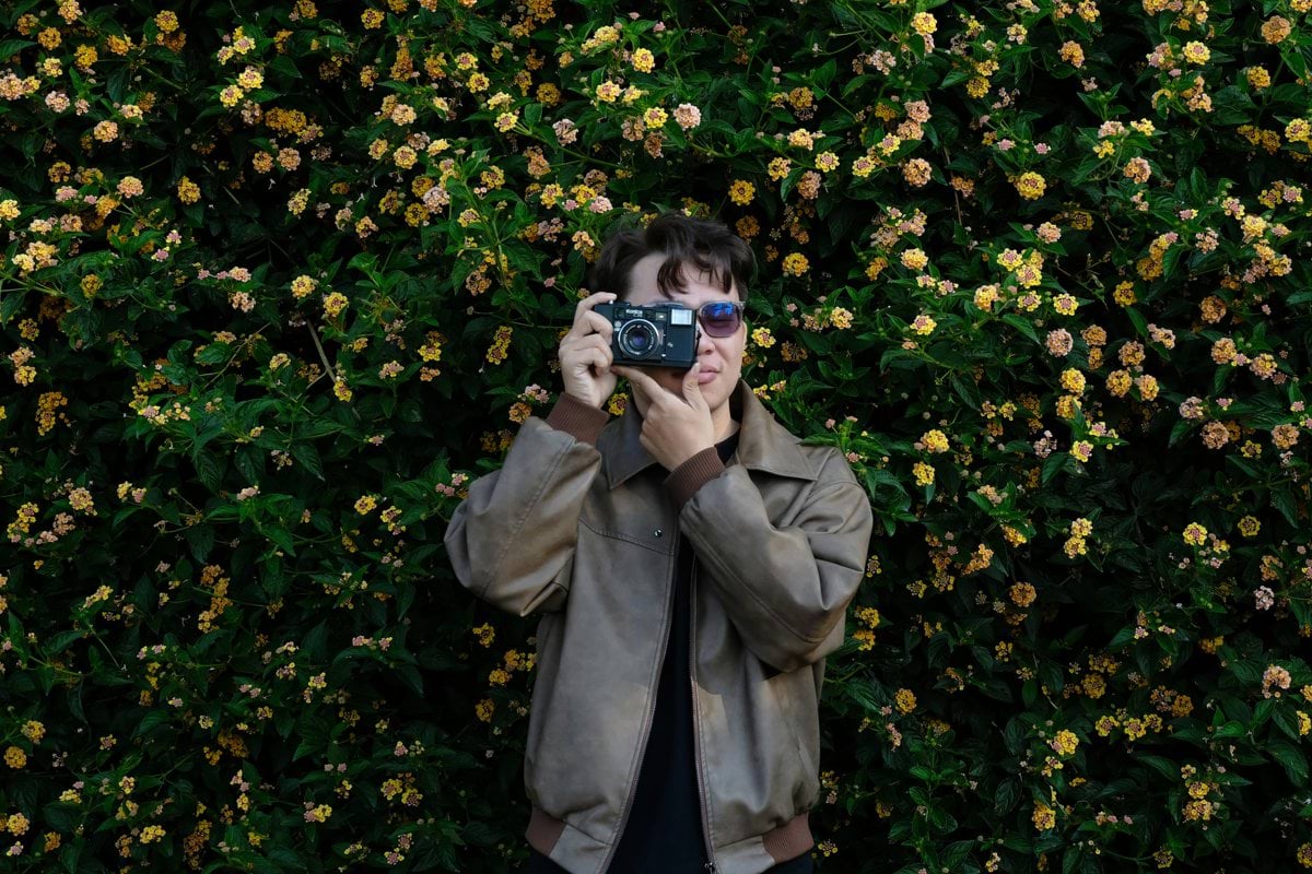 Person holding vintage camera in front of blooming flowers
