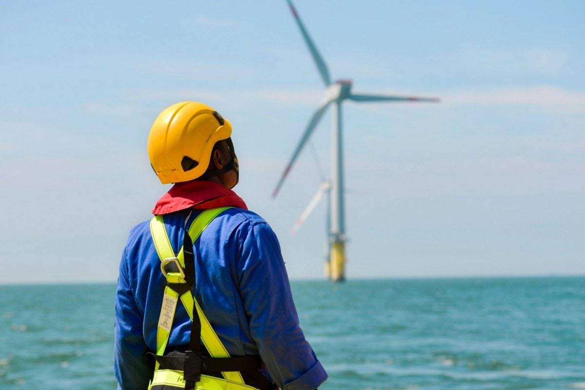 a man in a hard hat and safety gear looking at a wind turbine