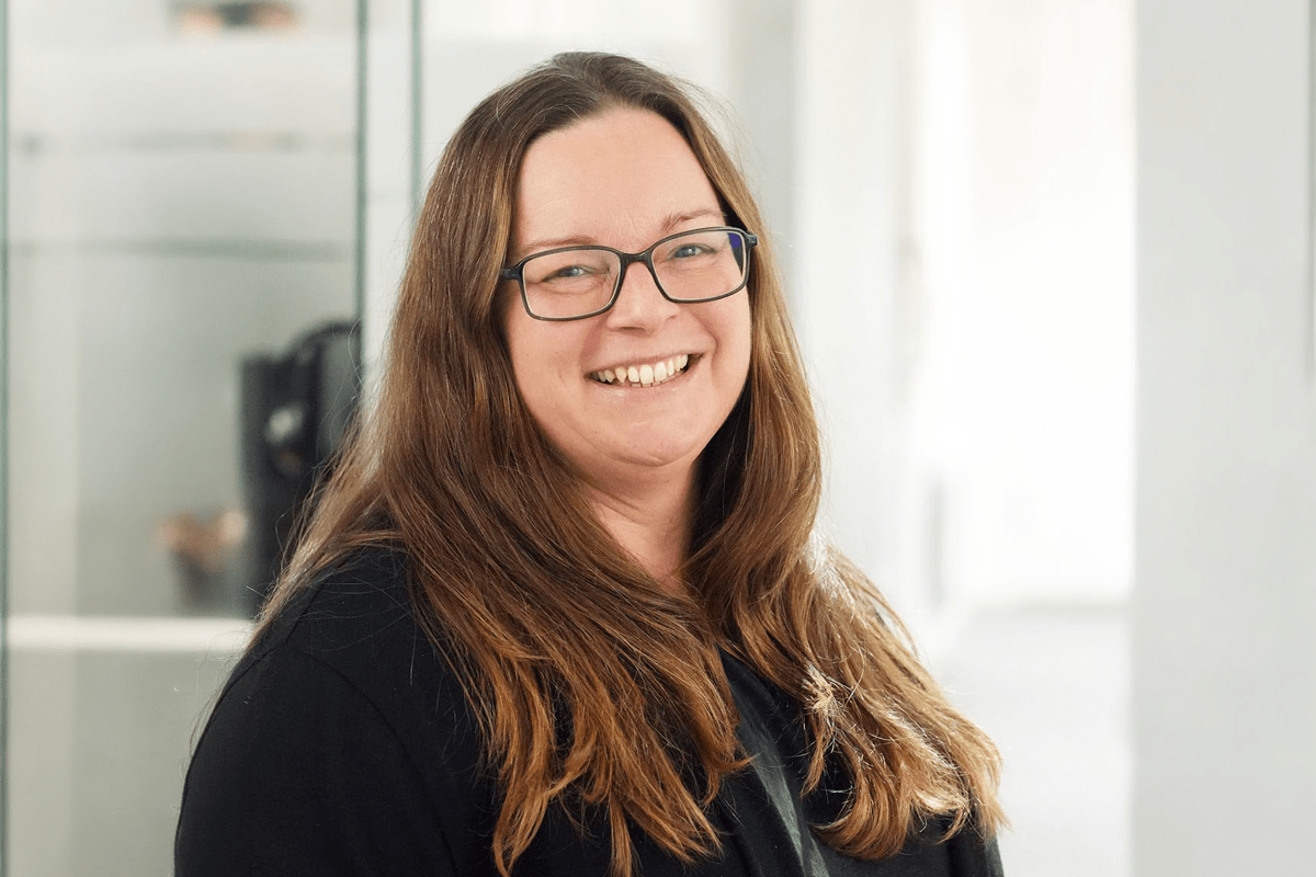 Kvinna med långt hår och glasögon ler in i kameran