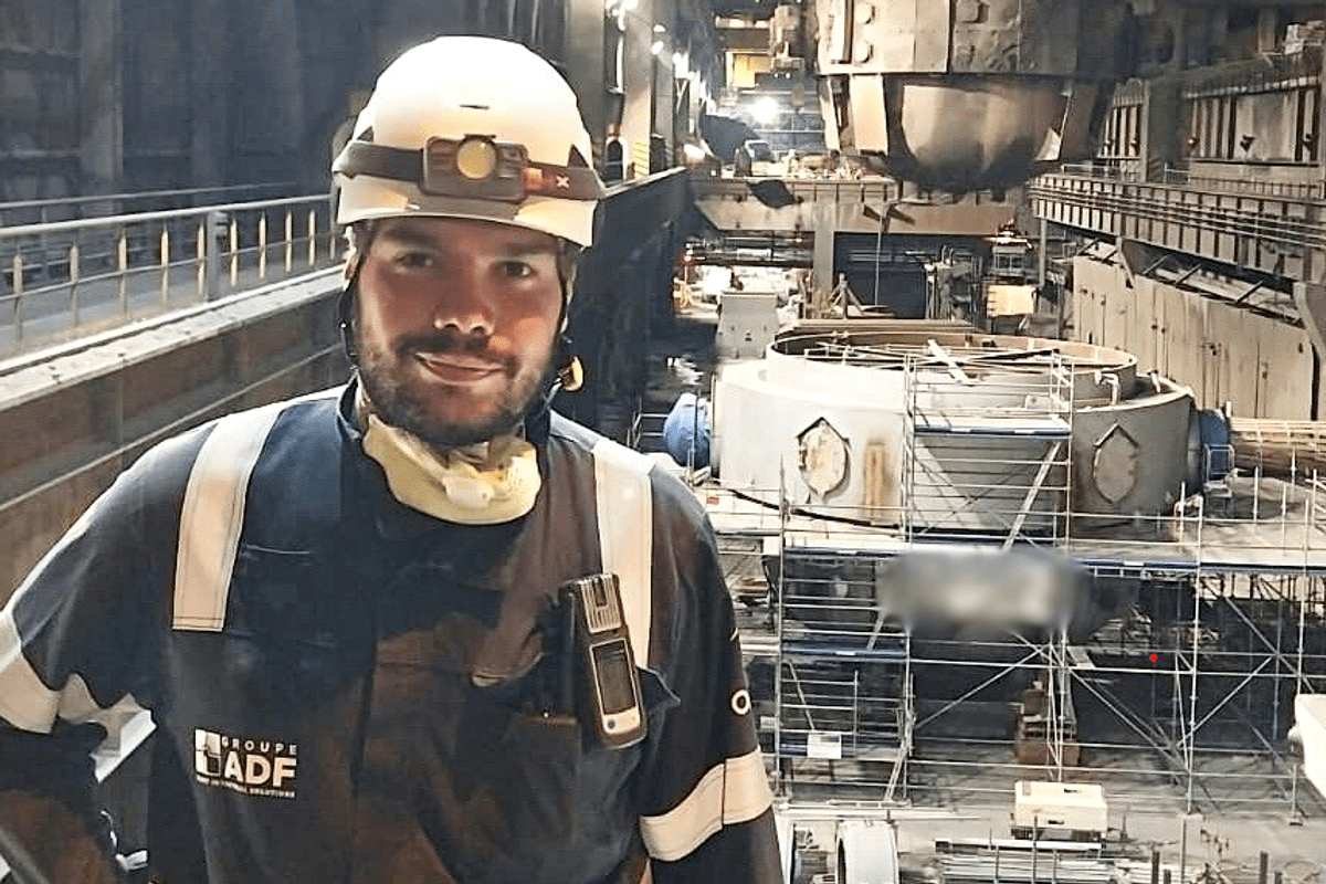 Portrait de la personne qui livre un témoignage, salarié en tenue de travail et casque de chantier, souriant devant une grande installation industrielle