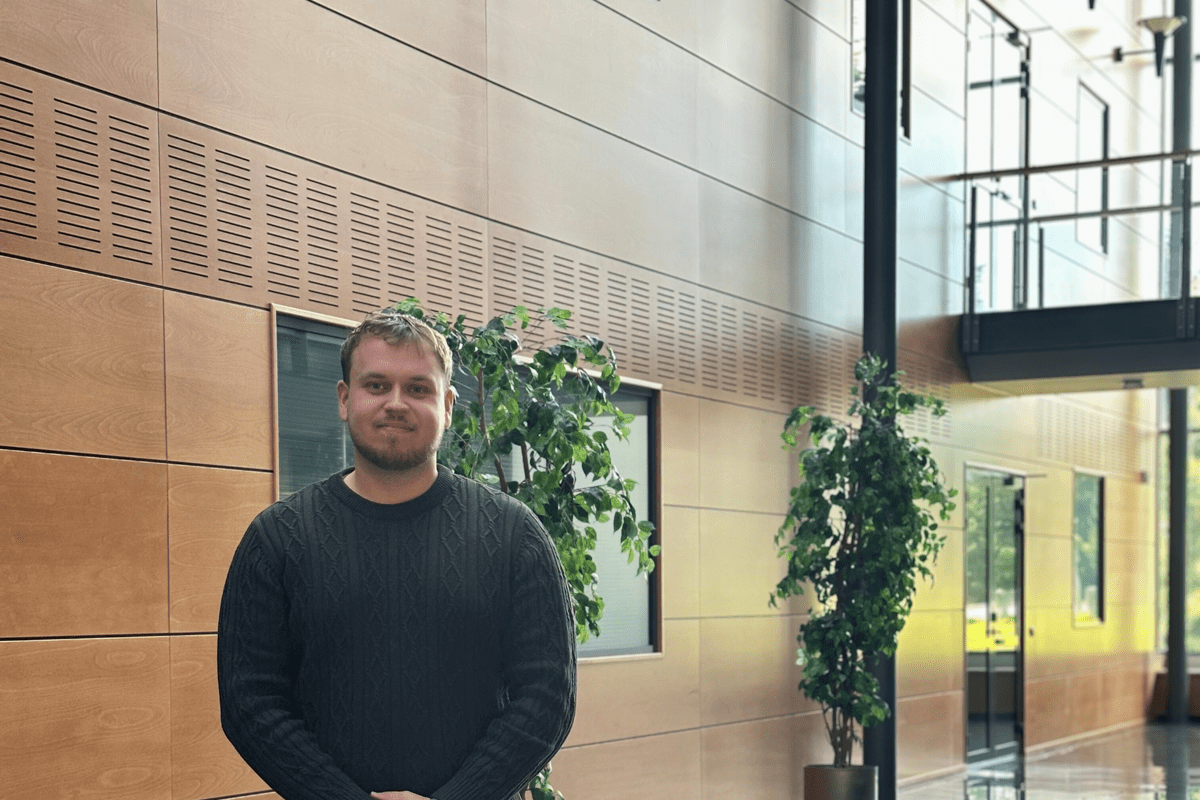 A man standing in a big office hall with green plants and sunlight