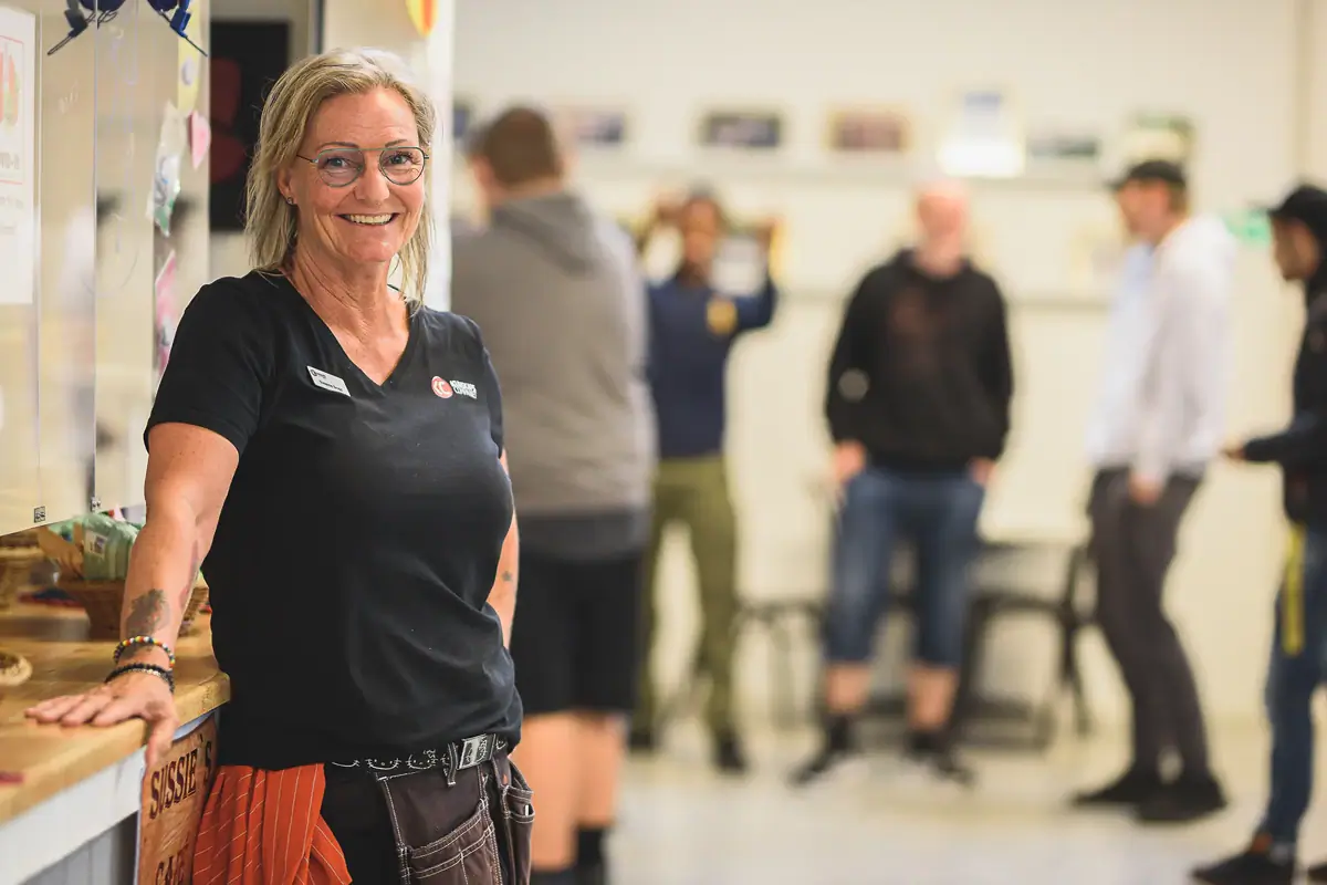 Leende kvinna i svart tröja står i en korridor med studenter.