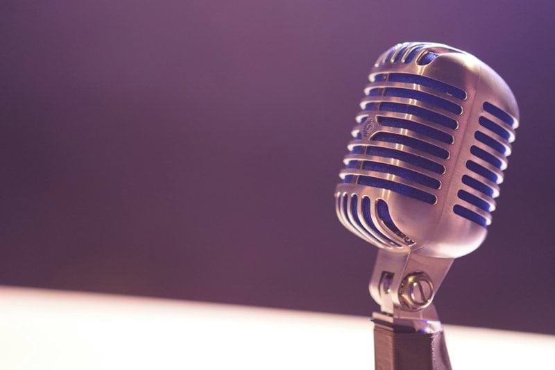 A vintage silver microphone with blue accents against a soft purple background