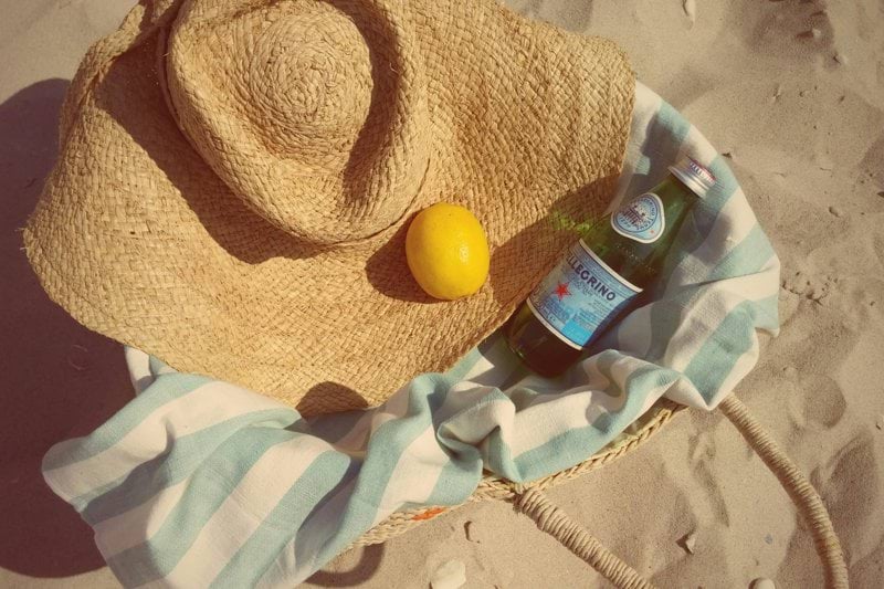 a hat and a bottle on a towel on the beach