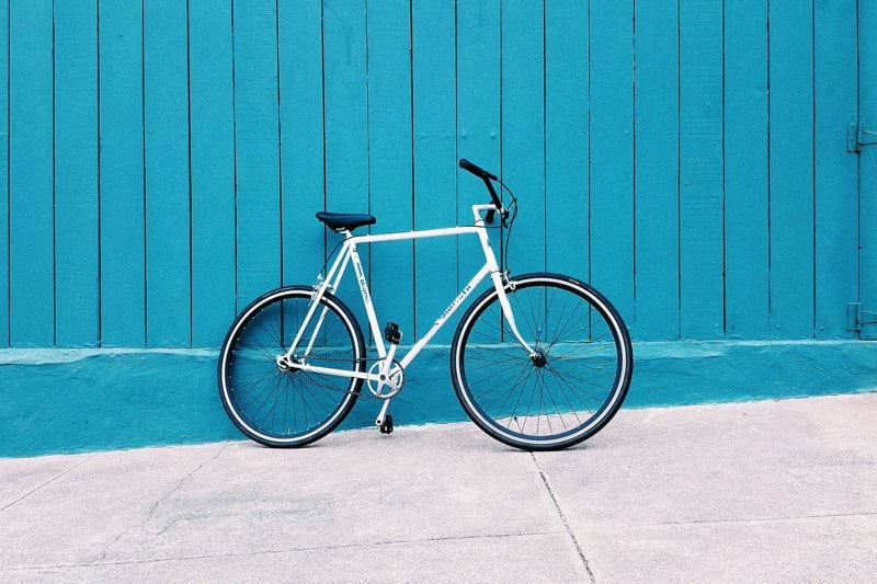 white road bike leaning on teal wooden wall during daytime