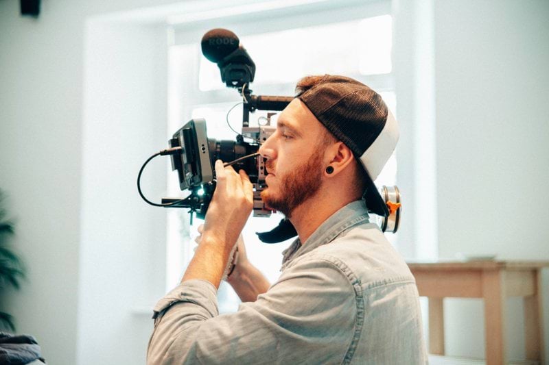 man wearing chambray shirt holding shoulder-mount camera