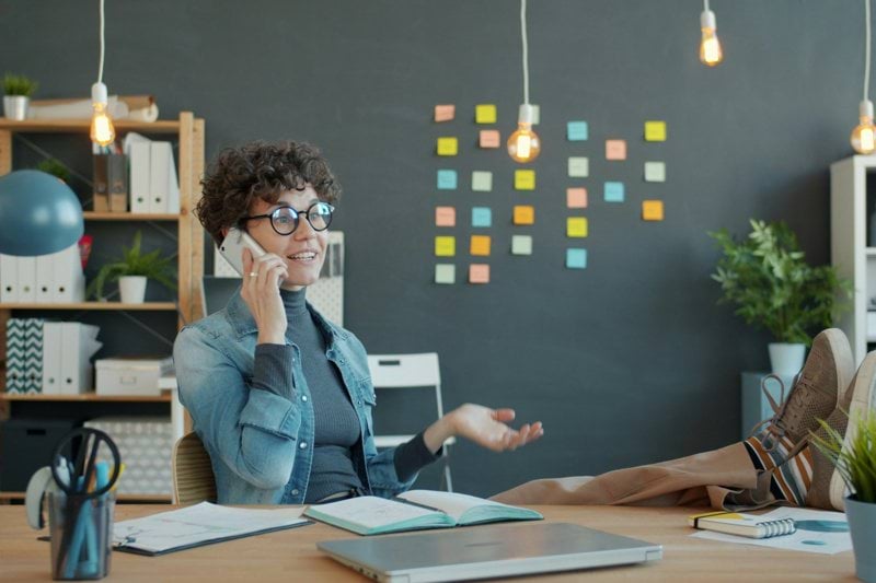 Woman talking on phone at desk with feet up