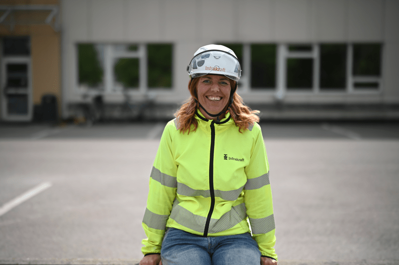 Porträttfoto på en leende kvinna i varseljacka och bygghjälm taget framifrån.