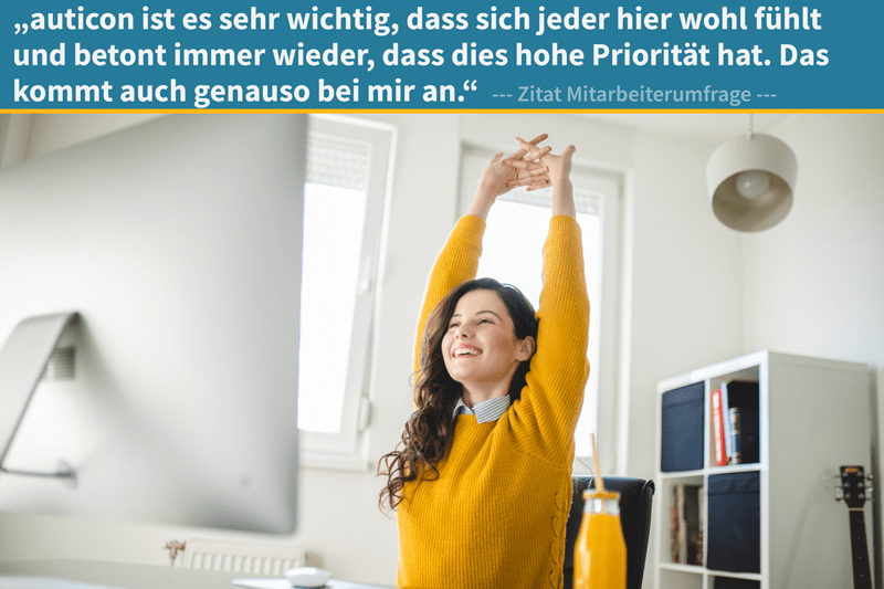 Eine Frau im gelben Pullover sitzt lächelnd am Schreibtisch und streckt sich entspannt. Die helle Umgebung vermittelt Wohlbefinden. Im Bild: ‚auticon legt großen Wert darauf, dass sich jeder wohlfühlt – das spüre ich auch so.