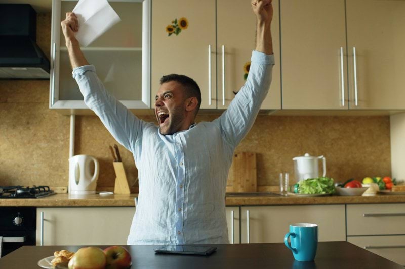 Man celebrating with arms raised in kitchen.