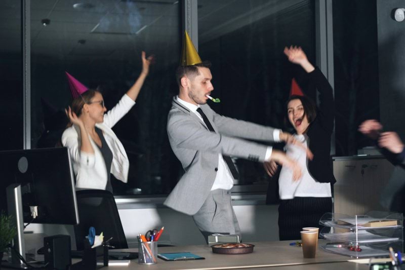 People in party hats dancing in an office at-work celebration.