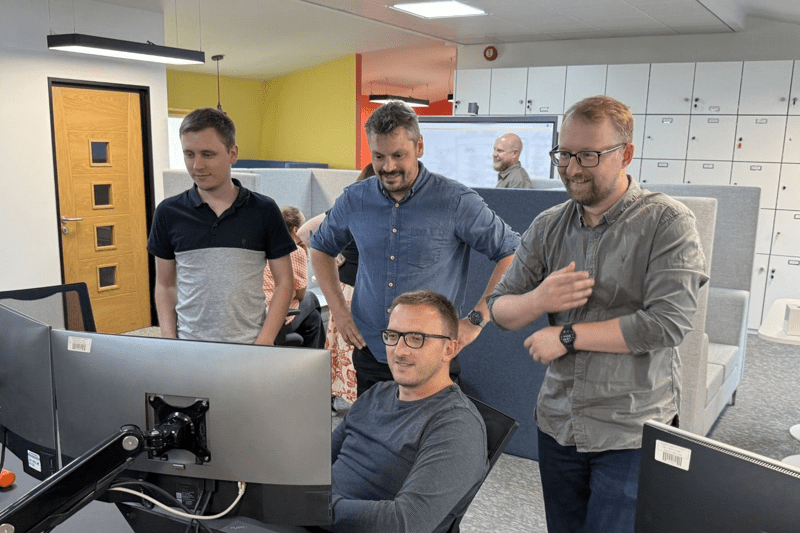 A group gathered together around a computer screen at a hackathon