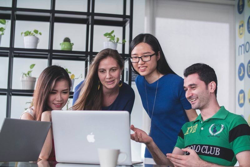 four people watching on white MacBook on top of glass-top table
