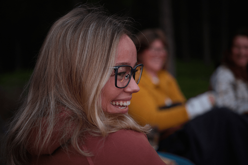 Kvinna som bär glasögon ler och man ser två kvinnor i bakgrunden