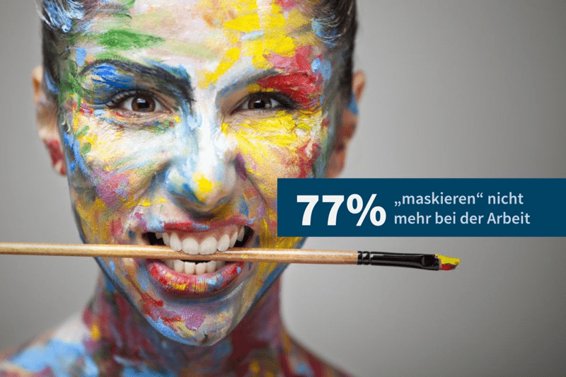 Eine lächelnde Frau mit bemaltem Gesicht hält einen Pinsel zwischen den Zähnen. Die Farben stehen für Facetten, die oft verborgen bleiben. Im Bild: „77 % maskieren nicht mehr bei der Arbeit– bei auticon können sie authentisch sein.“