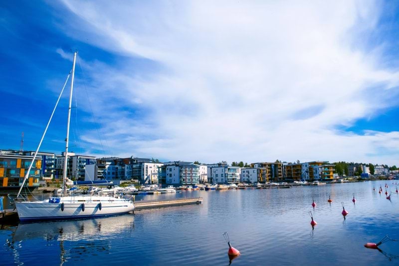 white and red boat on sea near city buildings under blue and white sunny cloudy sky