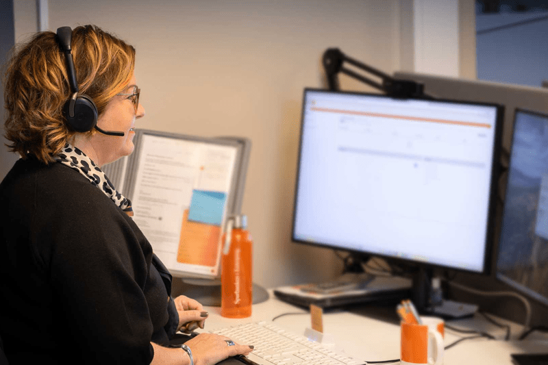 En kvinna med headset jobbar vid sin dator.