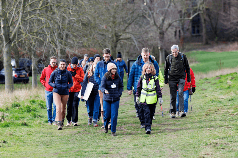 A group of walkers in outdoor clothing walk along a grassy path bordered by trees. Overlaid text reads “Communications & Campaigns.”