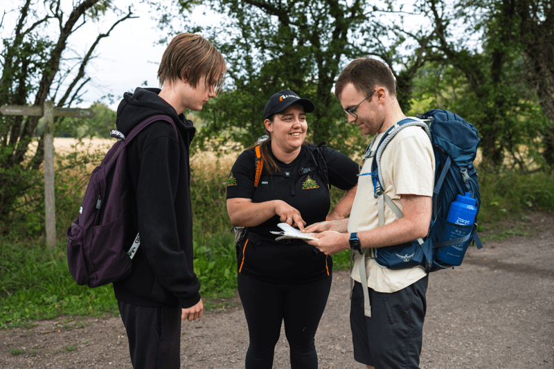 Three people with backpacks stand on a path outdoors, looking at a map. Overlaid text reads “Digital Transformation & Technology.”