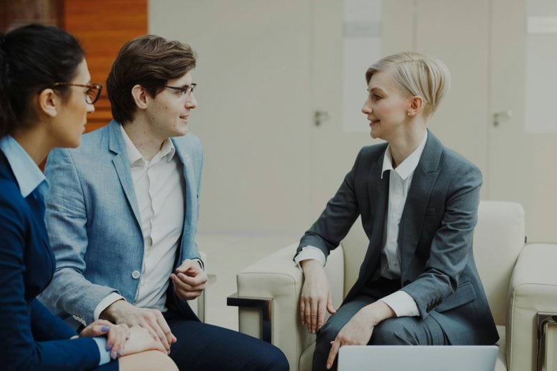 Three professionals in business attire conversing indoors