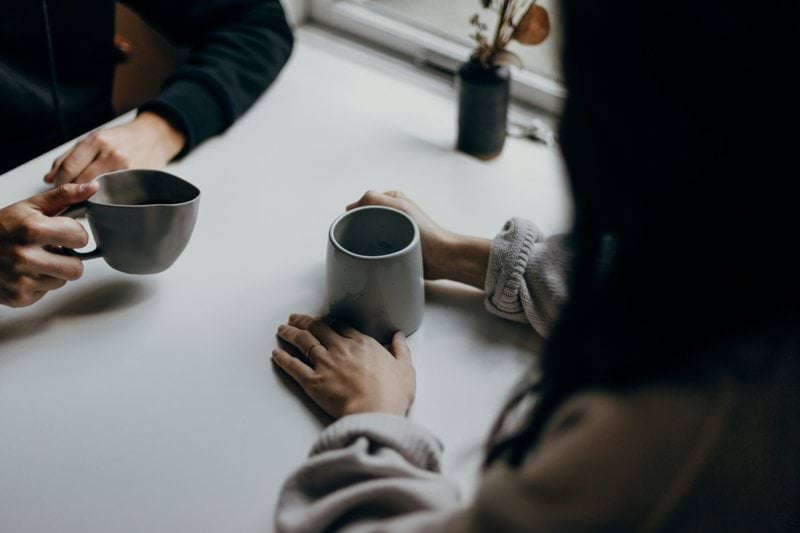 two people holding gray mugs at table