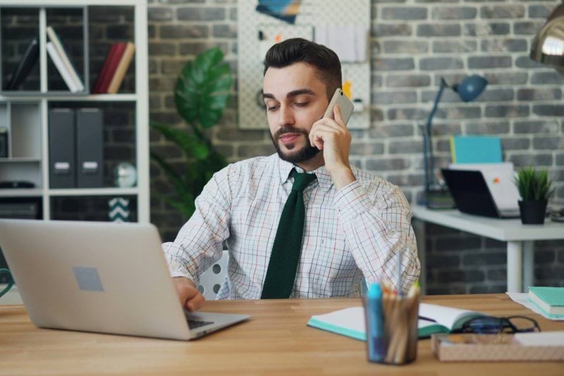 a man sitting in front of a laptop talking on a cell phone