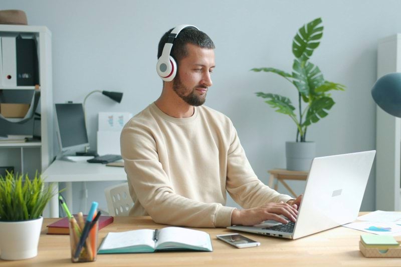 Man wearing headphones works on laptop at desk.