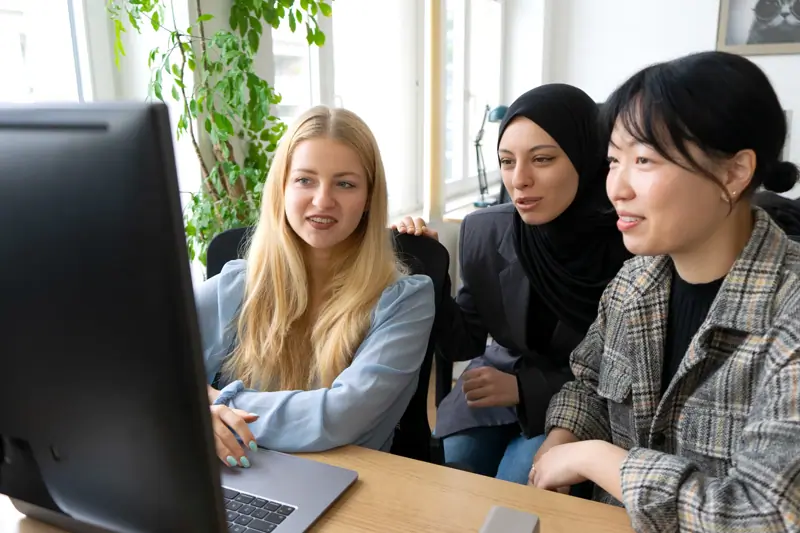 Three colleagues sitting together at a desk, collaborating while looking at a computer screen in an office.