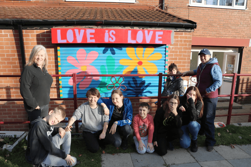 Young people stood in front of a colourful mural with the words 'love is love'
