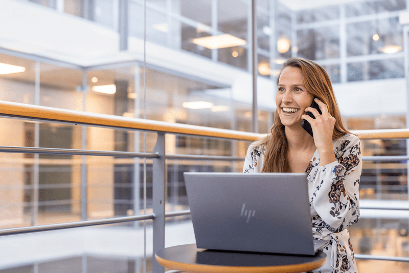 Leende medarbetare pratar i telefon framför datorn.