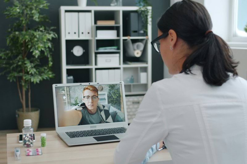 Doctor consulting patient via video call on laptop.
