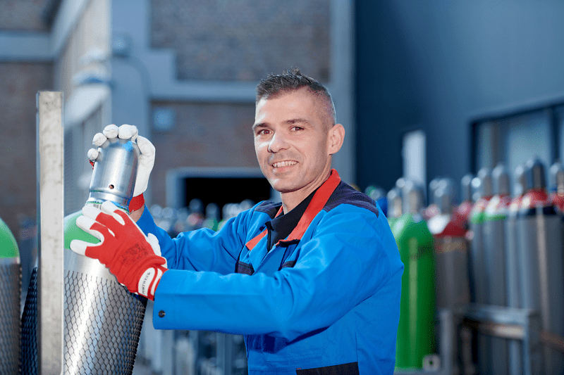 A man in blue work clothes and red safety gloves holds a cylinder, focused on his task.