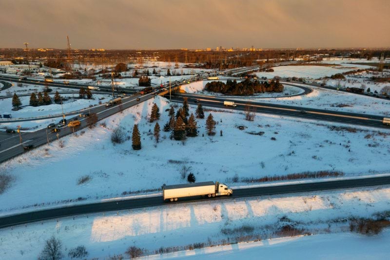 Semi-truck driving on a snowy highway at sunset.