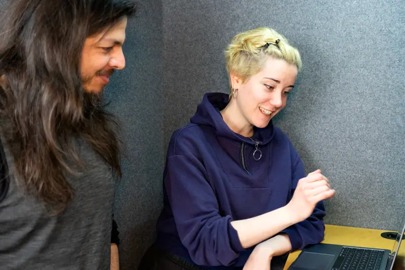 Two colleagues standing together and reviewing content on a laptop in an office.