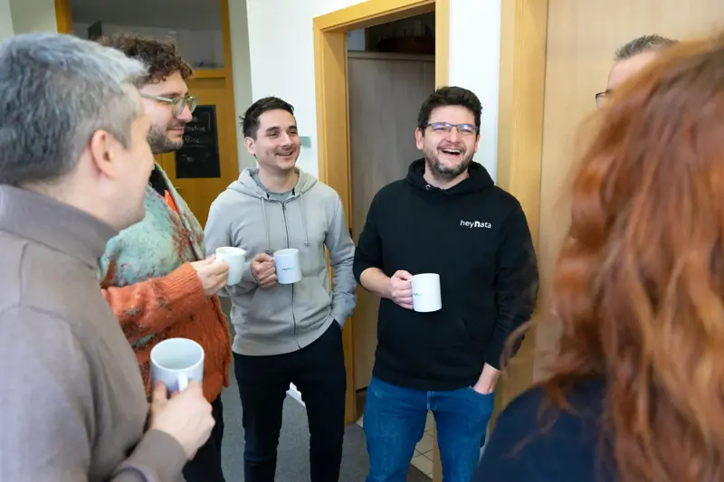 Colleagues standing together in an office hallway, chatting and holding coffee mugs.