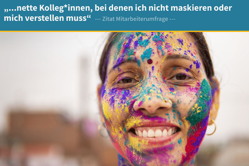 Eine lächelnde Frau mit buntem Farbpulver im Gesicht schaut in die Kamera. Die Farben symbolisieren Vielfalt und Individualität. Im Bild: ‚…nette Kolleg*innen, bei denen ich nicht maskieren oder mich verstellen muss.