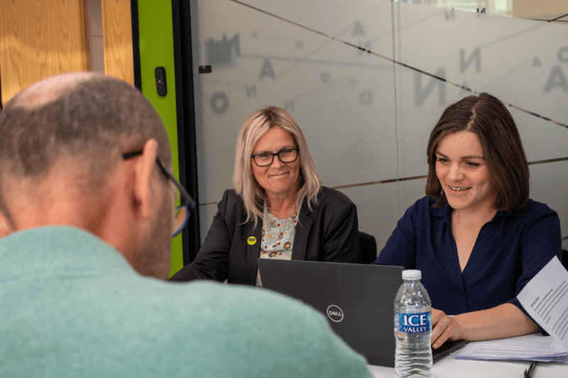 Members of our patient advisory group in a meeting - two women smiling and looking down at the desk