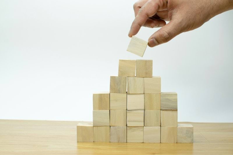 A hand is placing a piece of wood into a pyramid