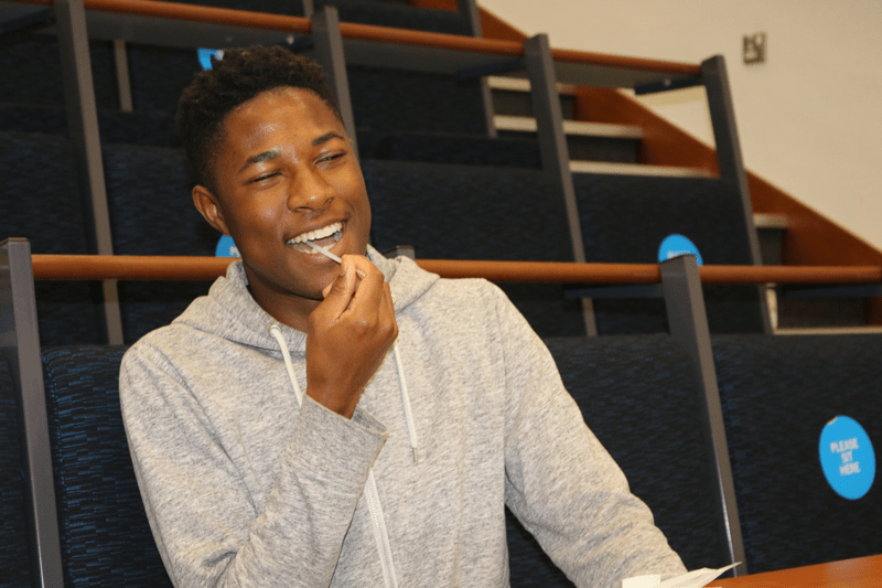 Young man smiling while swabbing his cheek to sign up to the stem cell register