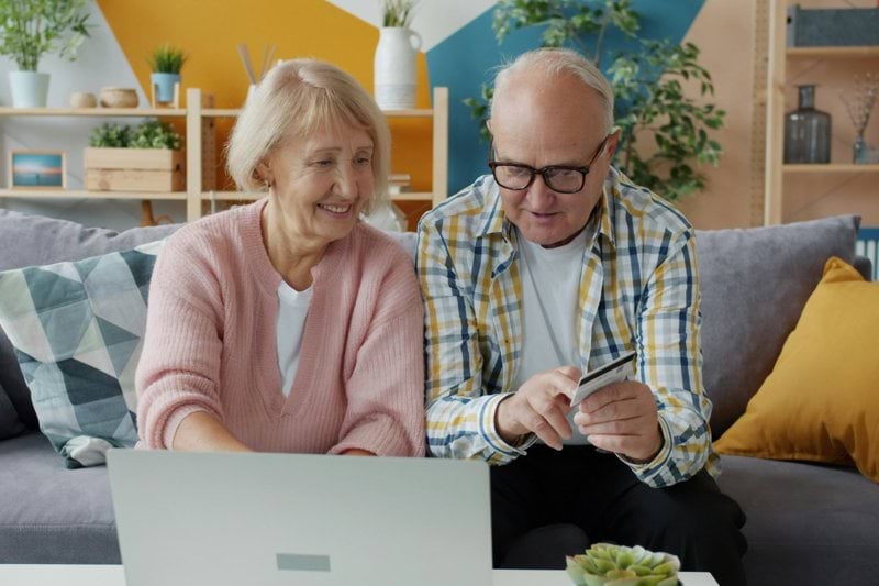 Elderly couple using laptop and credit card at home