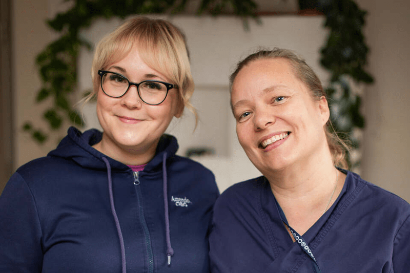 kaksi attendolaista hymyilee kameralle tummansinisissä työvaatteissa