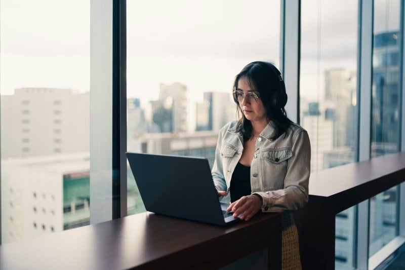 Woman wearing headphones working on a laptop by window