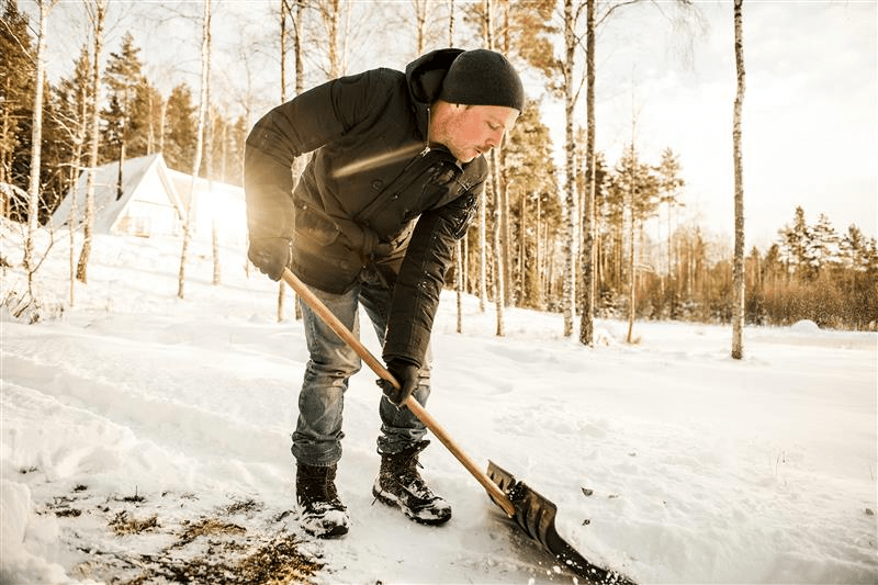 Personne en train de pelleter de la neige dans une forêt ensoleillée.