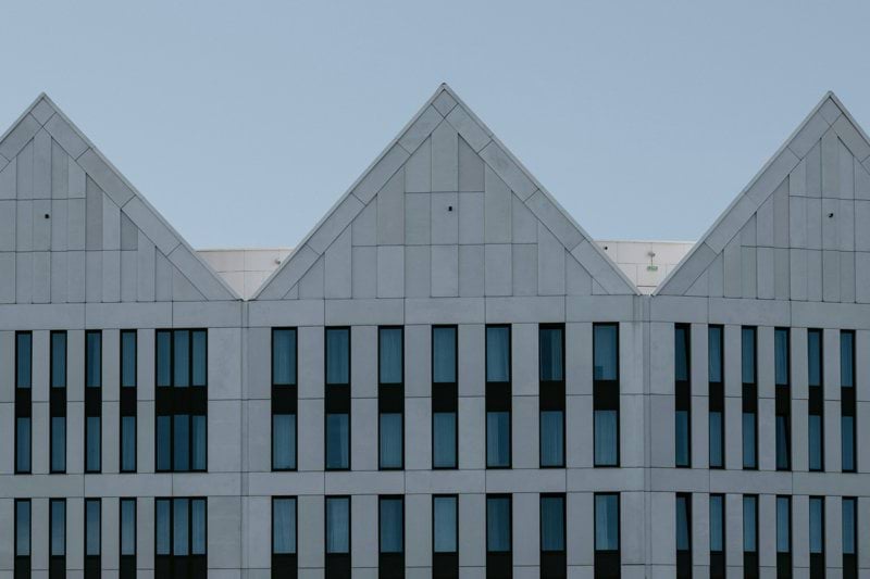 A modern building facade with three triangular gables and rows of rectangular windows