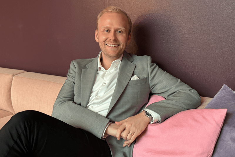 Gustaf porträtteras i sittandes i en soffa med ett leende på läpparna