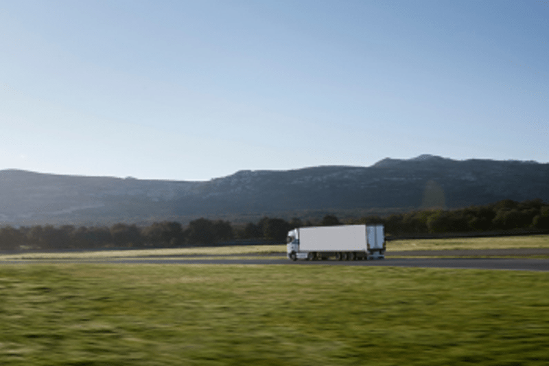 Truck driving along a rural road with mountains in the background.